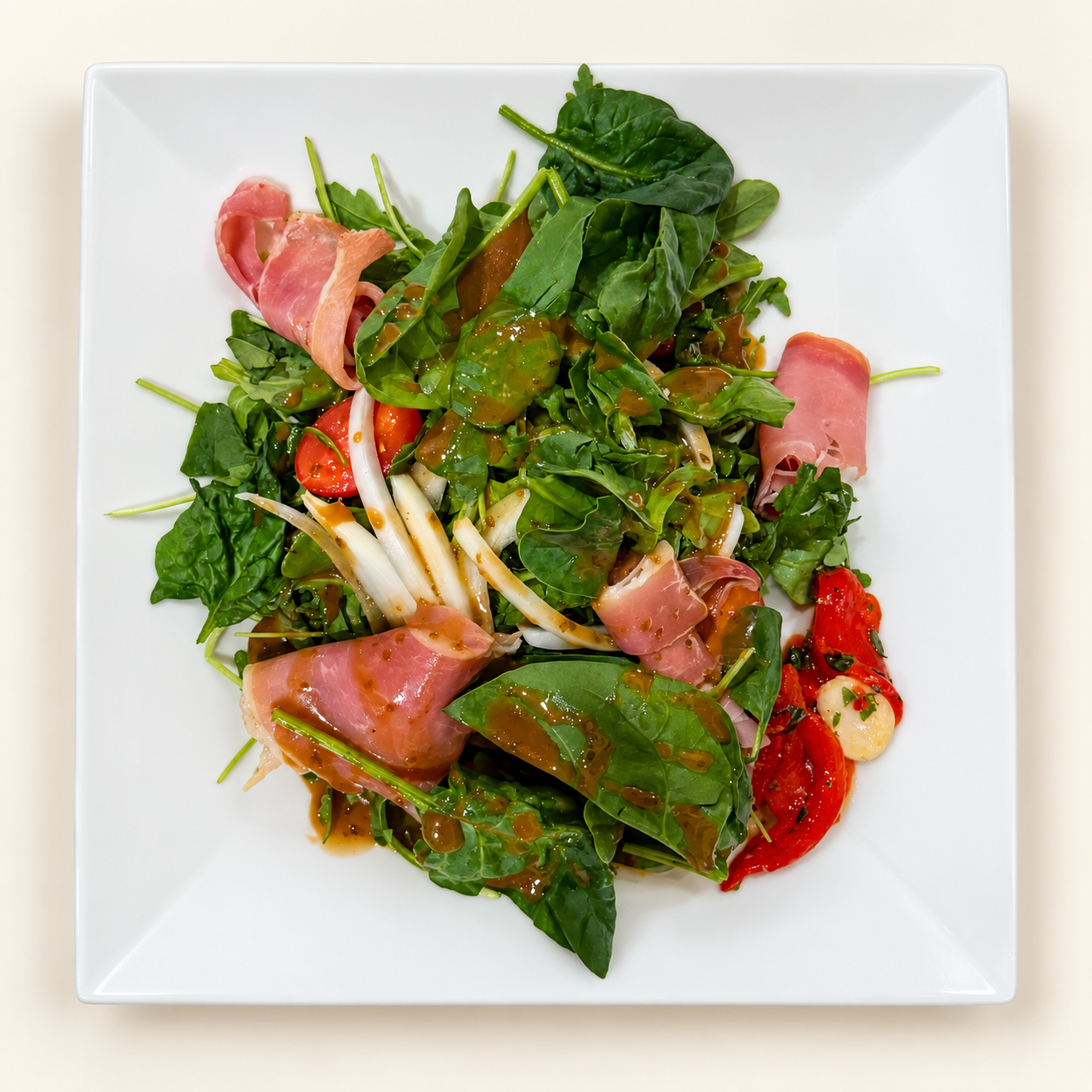 A salad with greens, tomatoes, onions and prosciutto